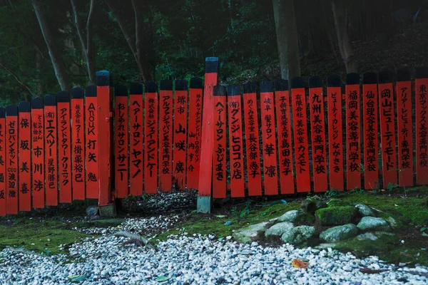Red fence with japanese text along forest and moss covered stones at Mikami-jinja Shrine in Kyoto, Japan