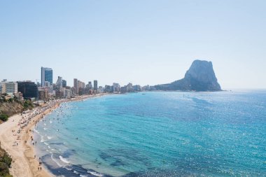 Tatil, yüzme ve güneşlenme için turistlerin bulunduğu yaz plajı Calpe kıyıları boyunca kaya oluşumu 'ifach', Costa Blanca, İspanya