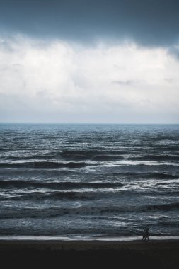 İspanya, Daimus 'ta fırtınalı, karanlık, parlak okyanus boyunca boş sahilde yürüyen bir çift.