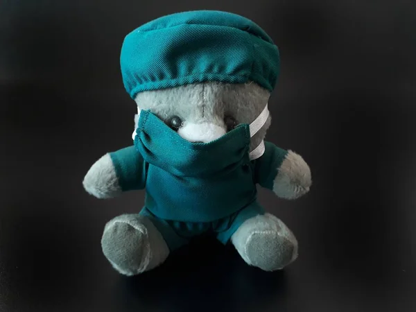 Siyah Arkaplan 'a sahip mavi renkli cerrah üniforması kullanan gri bir ayı bebeği. Oyuncak ayıyı yeşil renkli doktor kıyafetiyle izole ettim. Corona Virüs Salgınında Doktor Ameliyat Başı, Yüz Maskesi Kullanıyor. Doktor ameliyata hazır.