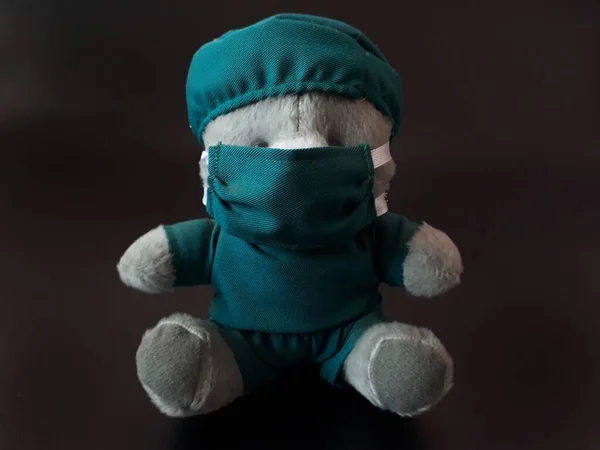 Siyah Arkaplan 'a sahip mavi renkli cerrah üniforması kullanan gri bir ayı bebeği. Oyuncak ayıyı yeşil renkli doktor kıyafetiyle izole ettim. Corona Virüs Salgınında Doktor Ameliyat Başı, Yüz Maskesi Kullanıyor