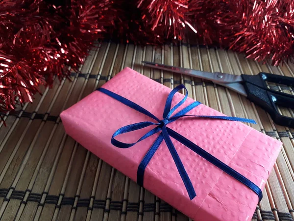 Mavi İnce Kurdeleli Pembe Hediye Kutusu. Tahta bambu üzerinde makaslı bir Noel hediyesi ve Red Tinsel. Yılın en güzel zamanlarında vermenin neşesi. Sevgililer Günü Hediyesi, Doğum günü Hediyesi.