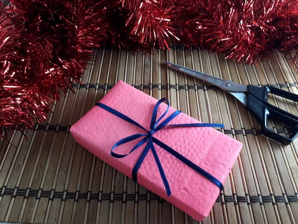 Mavi İnce Kurdeleli Pembe Hediye Kutusu. Tahta bambu üzerinde makaslı bir Noel hediyesi ve Red Tinsel. Yılın en güzel zamanlarında vermenin neşesi. Sevgililer Günü Hediyesi, Doğum günü Hediyesi.