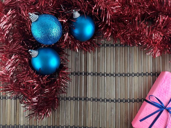 Kırmızı Tinsel, Mavi Baubles ve Mavi Kurdele ile sarılı Pembe Hediye Kutusu 'nun Düz Yatağı Görünümü. Noel Süslemeleri ve Bambu Arkaplanı ile Bulunan Boşluğu Kopyala