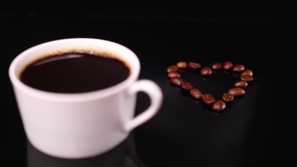 黒を基調とした白いコーヒーカップとハート型のローストビーンズ — ストック動画