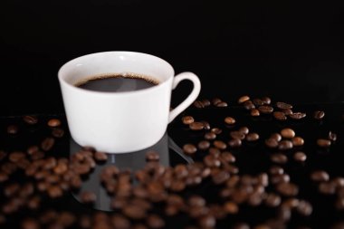 Kavrulmuş kahve çekirdekleri ve siyah arka planda beyaz bardak.