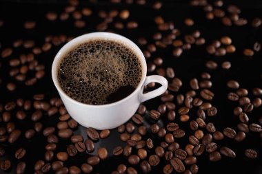 Kavrulmuş kahve çekirdekleri ve siyah arka planda beyaz bardak.