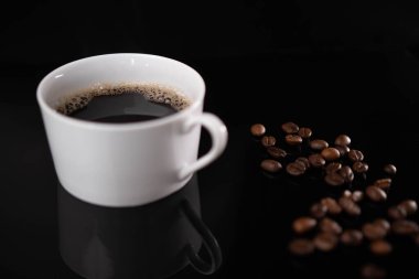 Kavrulmuş kahve çekirdekleri ve siyah arka planda beyaz bardak.