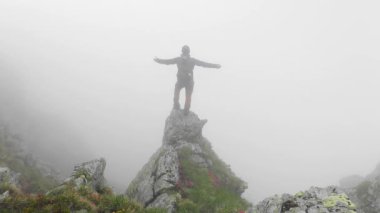 Dağdaki kayalıklarda sis ile yürüyen bir yürüyüşçüyle göz kamaştırıcı bir manzara.