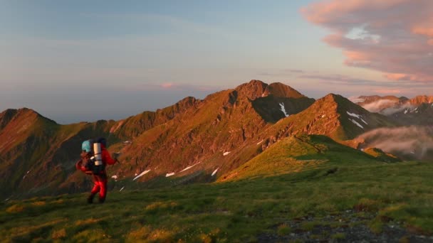 ソロハイカーは素晴らしい夕日の間に山の峰を歩く — ストック動画