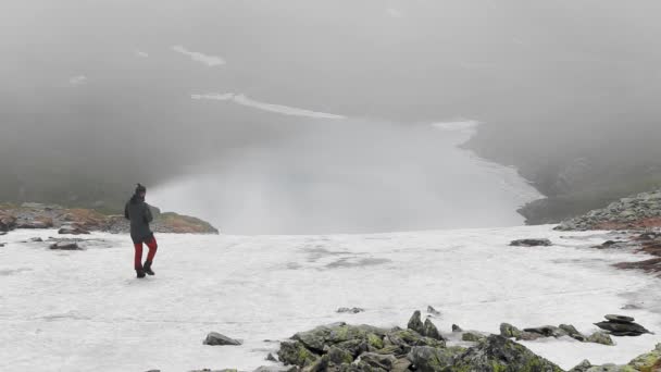Wędrowiec Siedzi Naprzeciwko Pięknego Jeziora Lodowca Śniegiem Mgłą — Wideo stockowe