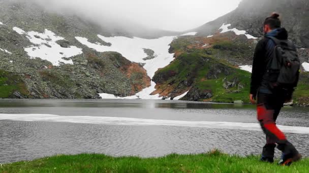 岩の多い山の氷河湖の近くを歩くハイカー — ストック動画