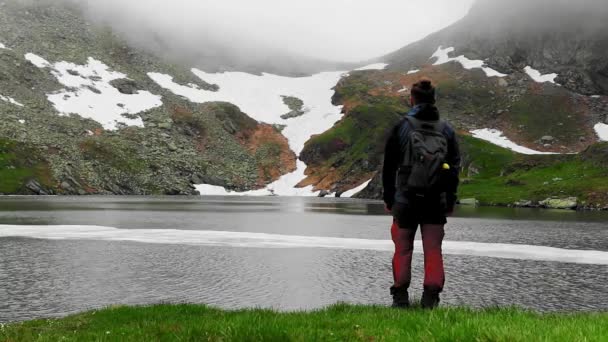 岩の多い山の氷河湖の近くを歩くハイカー — ストック動画