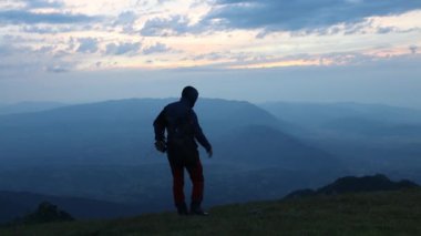 Bir adam tek başına oturur ve dağdan gelen çarpıcı günbatımına hayran kalır.
