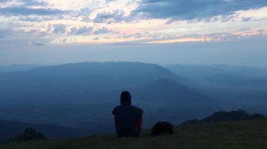 Bir adam tek başına oturur ve dağdan gelen çarpıcı günbatımına hayran kalır.