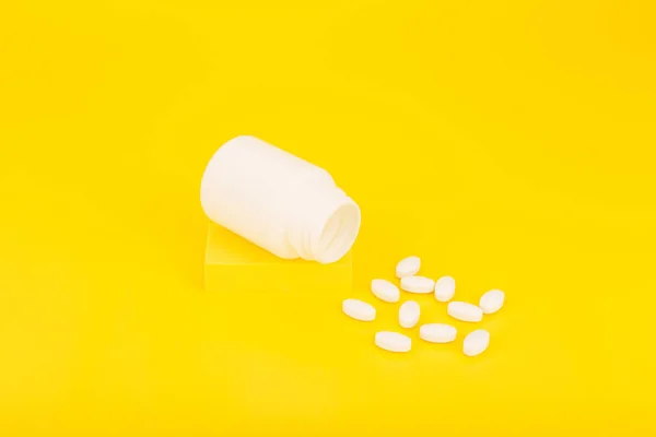 Botella de medicación abierta con pastillas derramadas en el podio contra el fondo amarillo —  Fotos de Stock