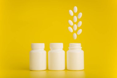 Üç beyaz ilaç şişesi. Sonuncusu sarı arka planda haplarla açılmış.