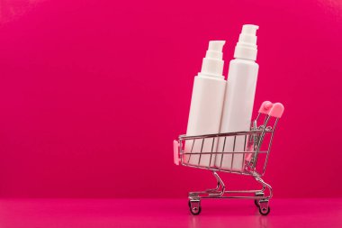 Pembe arka planda yüz kremleri ve metin için yeri olan alışveriş arabası.