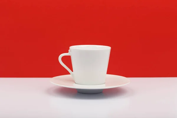 Λευκό φλιτζάνι καφέ ή τσάι σε λευκό τραπέζι με φόντο το κόκκινο — Φωτογραφία Αρχείου