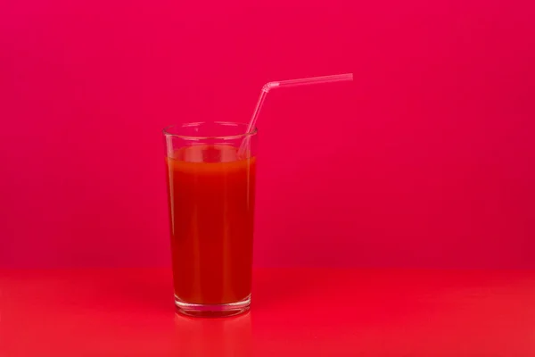 Tomatjuice i glas med sugrör mot röd bakgrund med textutrymme — Stockfoto