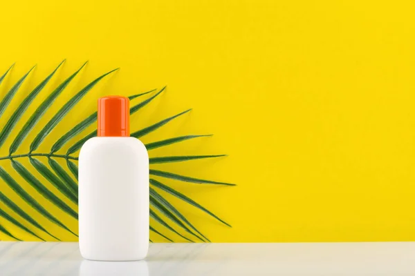 Sunscreen lotion in white jar with orange cap against yellow background with a palm with space for text — Stock Photo, Image