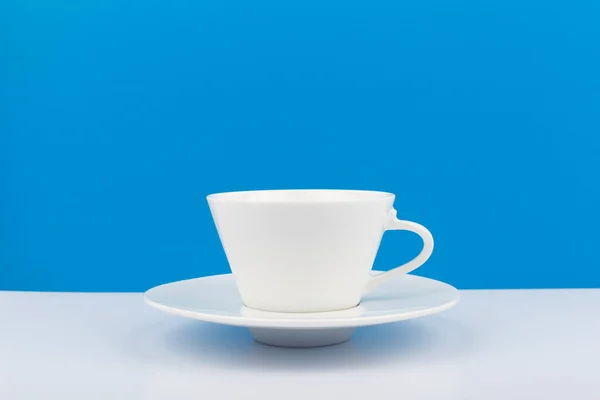 흰 세라믹 커피 잔과 파란 배경에 흰 탁자 위에 놓인 접시가 있는 — 스톡 사진