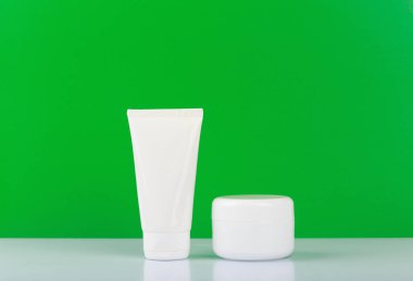 Beyaz parlak masa üzerinde yüz ve el kremi ile yeşil arkaplan arasında metin için yer var. 