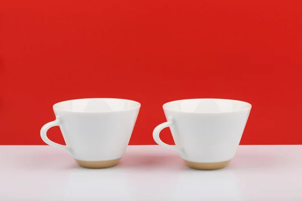 Dos tazas de café de cerámica blanca sobre mesa blanca sobre fondo rojo con espacio para texto —  Fotos de Stock