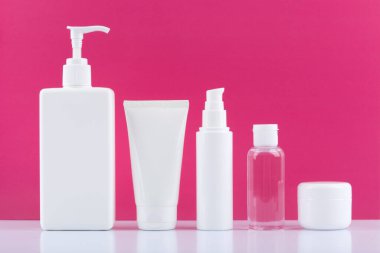 Vücut kremi, yüz kremi, temizlik köpüğü, losyon ve beyaz masanın altında parlak pembe arka plana karşı krem.