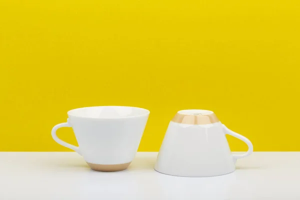 Duas xícaras de café de cerâmica branca na mesa branca contra fundo amarelo brilhante com espaço para texto — Fotografia de Stock