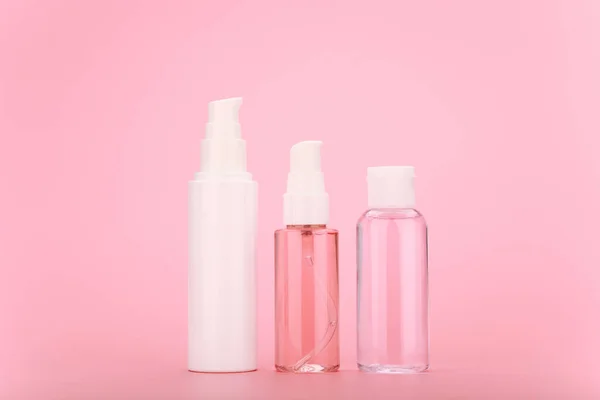 Gesichtscreme, Reinigungsschaum oder Gel und Lotion in transparenter Flasche mit weißen Verschlüssen vor leuchtend rosa Hintergrund — Stockfoto