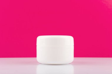 Beyaz krema kavanozu, parlak masa üzerinde, pembe arka planda fotokopi alanı ile. Güzellik ve cilt bakımı