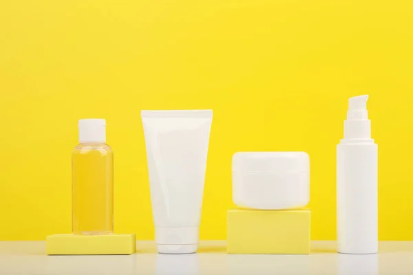 Set of cosmetic containers on white glossy table against bright yellow background.