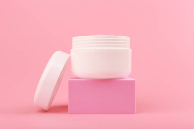 Yüz kremini kapat. Maske ya da merhem beyaz kavanozda pembe arka planda pembe podyumda açık kapaklı