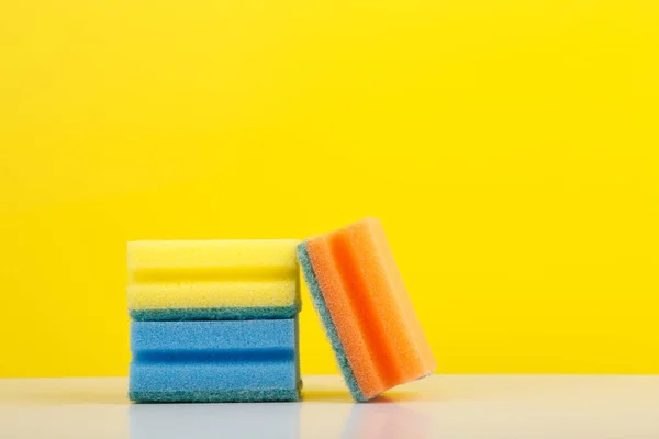 Éponges colorées pour laver la vaisselle sur table blanche sur fond jaune avec espace de copie — Photo