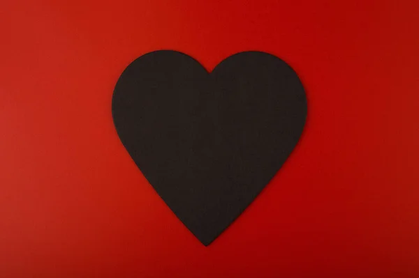 Nahaufnahme eines schwarzen Papierherzens vor rotem Hintergrund mit Kopierraum. Minimalistisches Konzept zum Valentinstag — Stockfoto