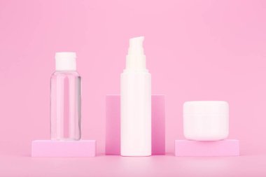 Pembe arka planda pembe kürsüde duran kozmetik şişeleri. Güzellik ürünleri ve günlük cilt rutini kavramı