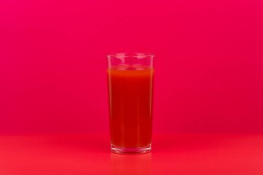 Kırmızı masada bir bardak domates suyu. Fotokopi çekilen pembe arka plana karşı. Vejetaryen yemeği ve sağlıklı yemek kavramı