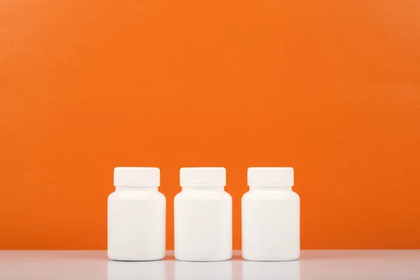 Three white medication bottles in a row against orange background with copy space. Vitamin C concept