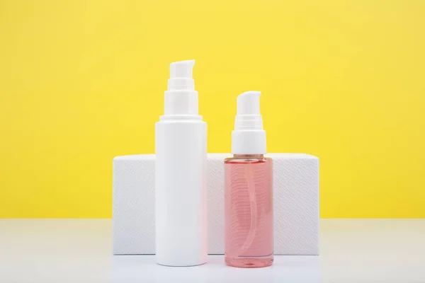 Creme facial em tubo branco e espuma de limpeza rosa em tubo transparente contra fundo amarelo com espaço de cópia. — Fotografia de Stock