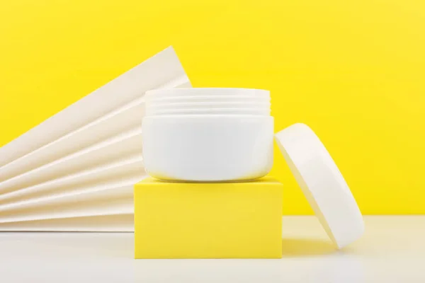 Close up de frasco aberto branco na mesa branca contra fundo amarelo decorado com waver branco — Fotografia de Stock