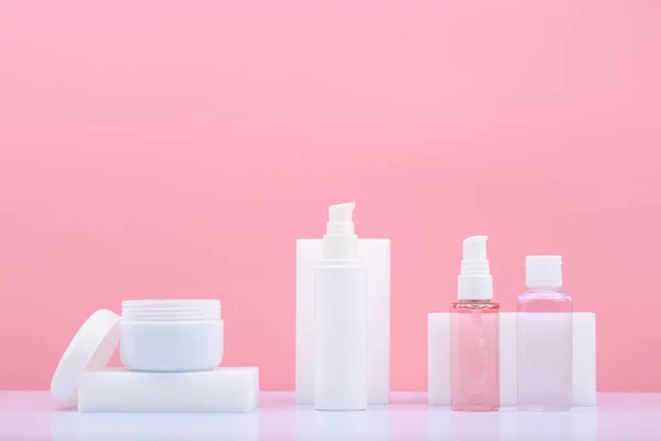 Kosmetikset zur Hautpflege in weißen Tuben auf weißem Tisch vor leuchtend rosa Hintergrund mit Kopierraum — Stockfoto