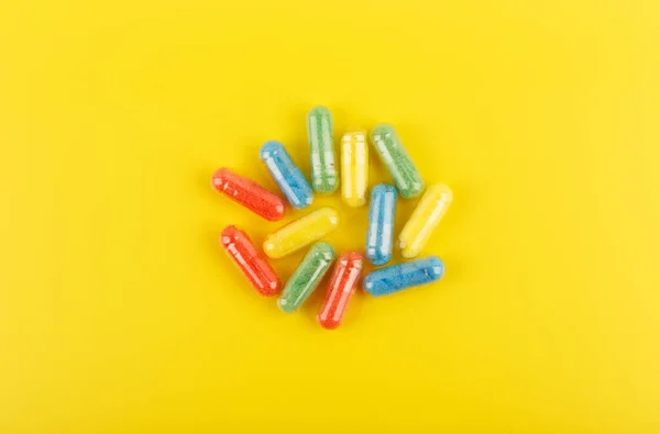 Vista ad alto angolo di pillole ovali multicolori contro lo sfondo giallo. Concetto di vitamine e benessere — Foto Stock