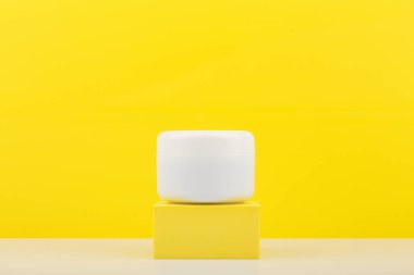 Sarı kaideye karşı beyaz kozmetik kavanoz, kopyalama alanı olan sarı arkaplan