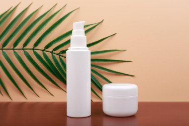 Seçici odak, el kremi ile kozmetik set ve bej arka planda palmiye yaprağı ile tırnak yağı