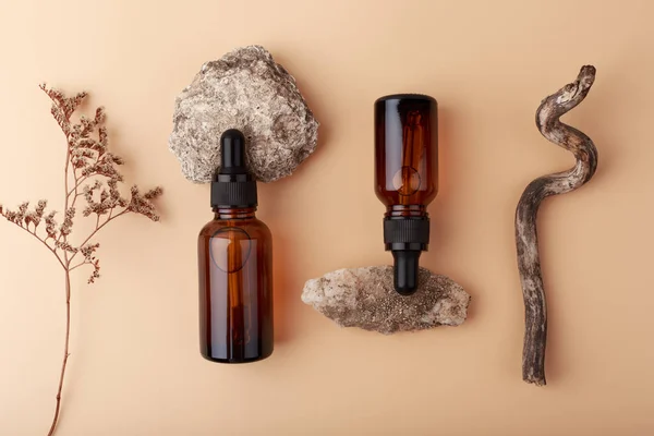 Vista superior de sueros de piel en botellas oscuras sobre fondo beige con piedras y flores secas —  Fotos de Stock