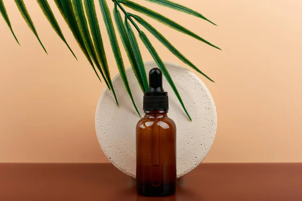 Skin serum in dark bottle with round gypsum circle with palm leaf against beige background — Stock Photo, Image