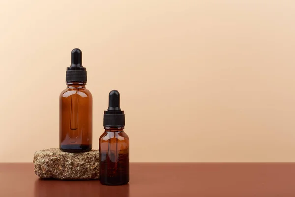 Two skin serums in dark bottles on brown table against beige background with copy space — Stock Photo, Image