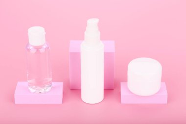 Pembe arkaplanda pembe geometrik podyumlarla kozmetik ürünlerinin yüksek açılı görüntüsü