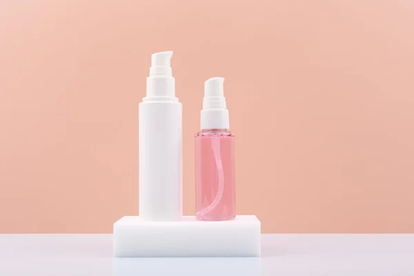 Tubos cosméticos com creme facial e gel líquido ou espuma para limpeza da pele no pedestal branco contra fundo rosa — Fotografia de Stock